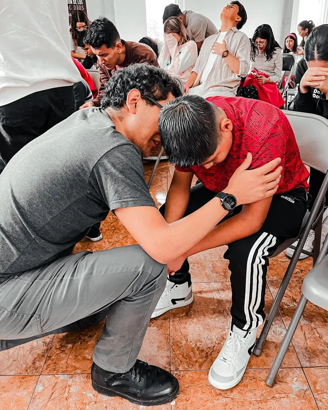 Un joven ora por otro que está sentado