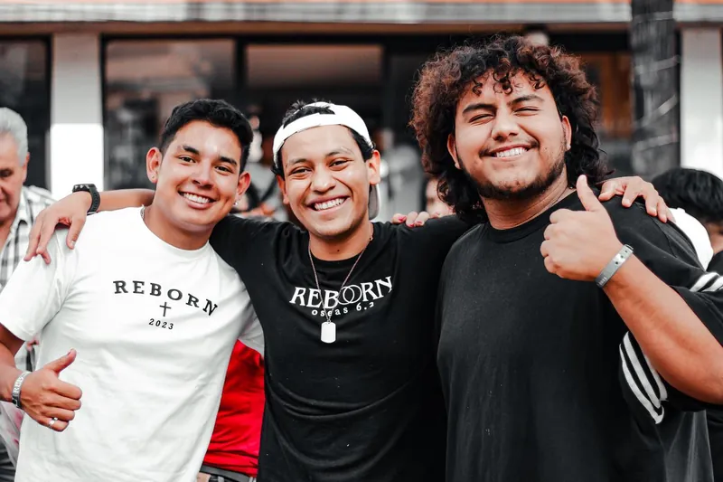 Tres jóvenes sonríen abrazados con playeras de REBORN
