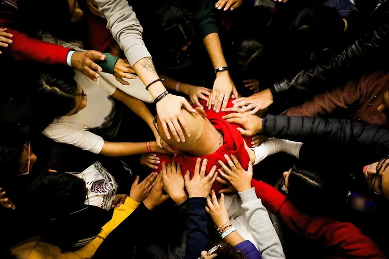 Jóvenes ponen la mano sobre un compañero para orar por él