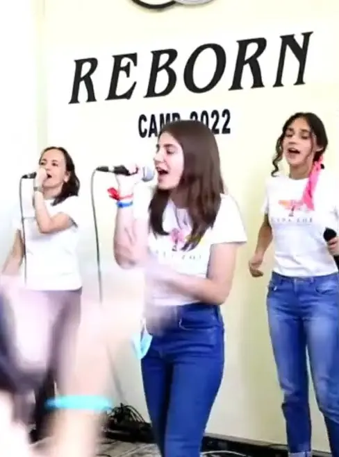 Tres jóvenes cantan en la alabanza de bienvenida de REBORN 2022, frente al letrero «REBORN CAMP-2022».